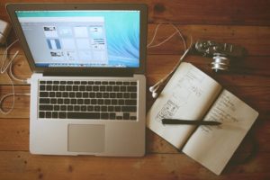 turned on laptop beside a ruled notebook and pen
