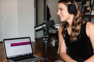 woman with headphones talking into microphone in front of laptop