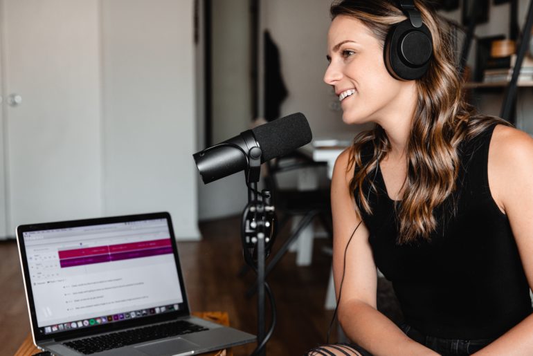 woman with headphones talking into microphone in front of laptop